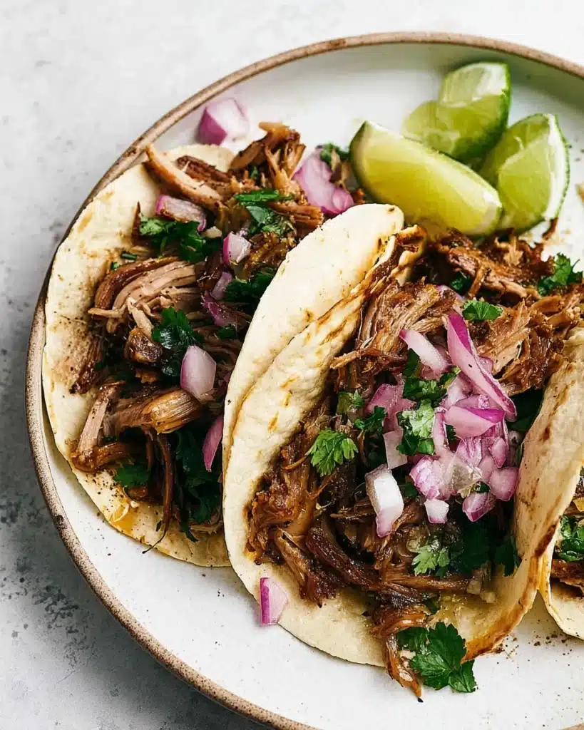 Slow Cooker Carnitas Tacos (Juicy, Crispy, and Easy) 4 Carnitas tacos with crispy pork, red onion, and cilantro on plate