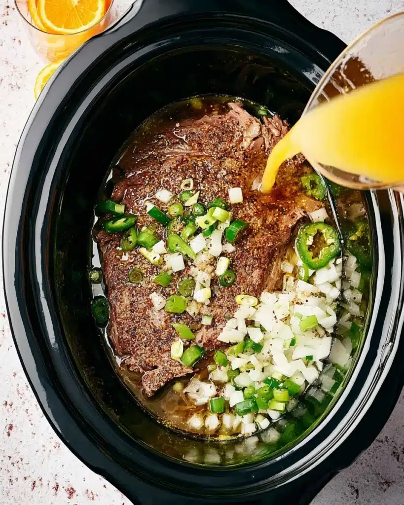 Slow Cooker Carnitas Tacos (Juicy, Crispy, and Easy) 2 Pork shoulder with onions and jalapeรฑos in slow cooker for carnitas tacos