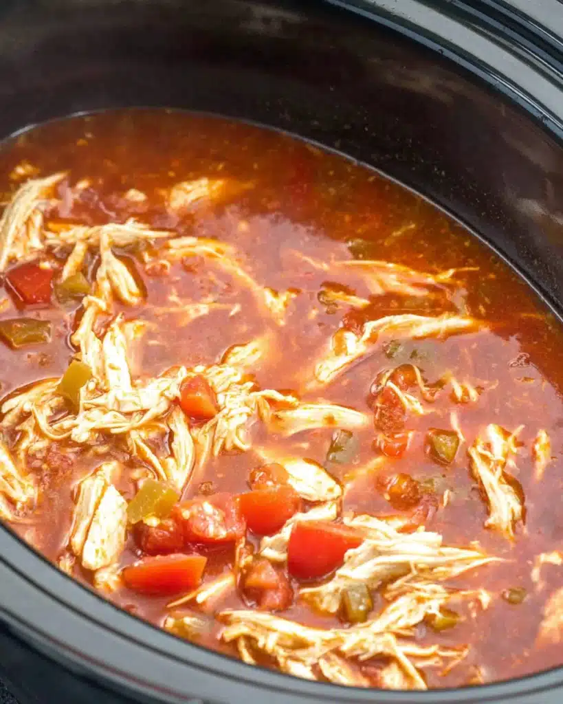 Slow Cooker Chicken Enchilada Casserole 4 Shredded chicken simmering in enchilada sauce inside a slow cooker