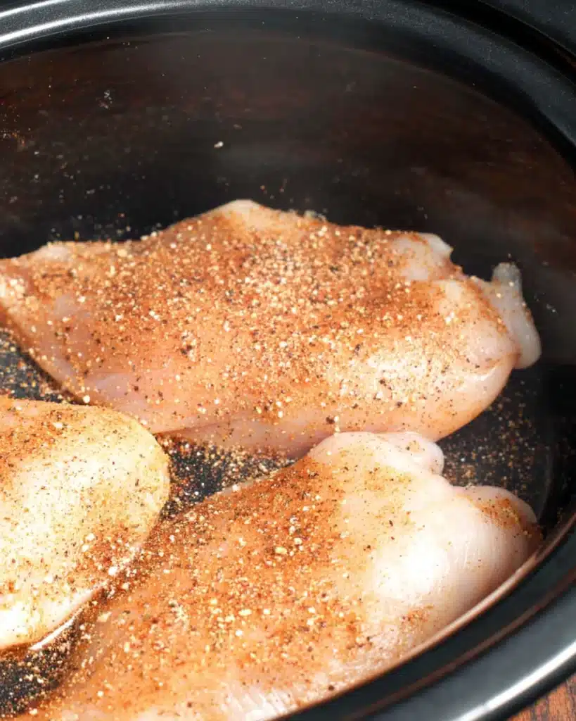Slow Cooker Chicken Enchilada Casserole 2 Raw chicken breasts seasoned with taco mix in a slow cooker for chicken enchilada casserole