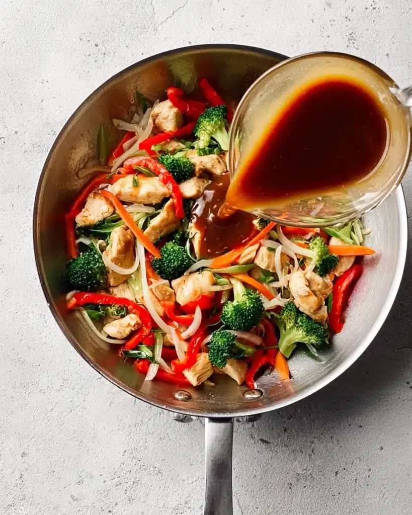 Easy Chicken Stir Fry (Quick, Flavorful, and Perfect for Busy Nights) 3 Pouring stir fry sauce over chicken and vegetables in a skillet
