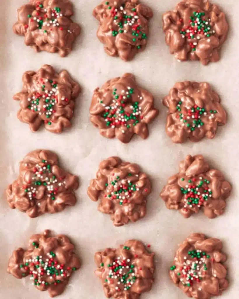 Christmas Crock Pot Candy clusters topped with red and green sprinkles on parchment