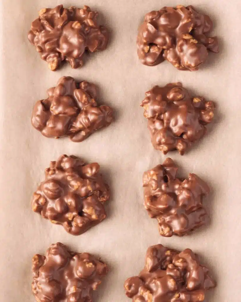 Scooped chocolate peanut clusters cooling on parchment for Christmas Crock Pot Candy