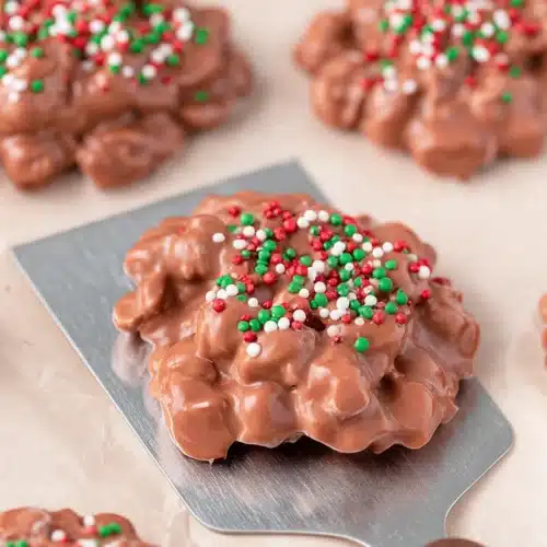 Christmas Crock Pot Candy clusters topped with red and green sprinkles on parchment paper