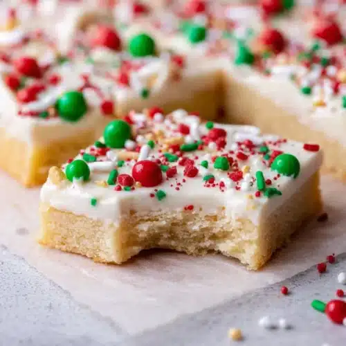 Christmas Sugar Cookie Bars (Soft, Chewy & Frosted) 7 Soft Christmas sugar cookie bars with white frosting and colorful sprinkles on marble surface