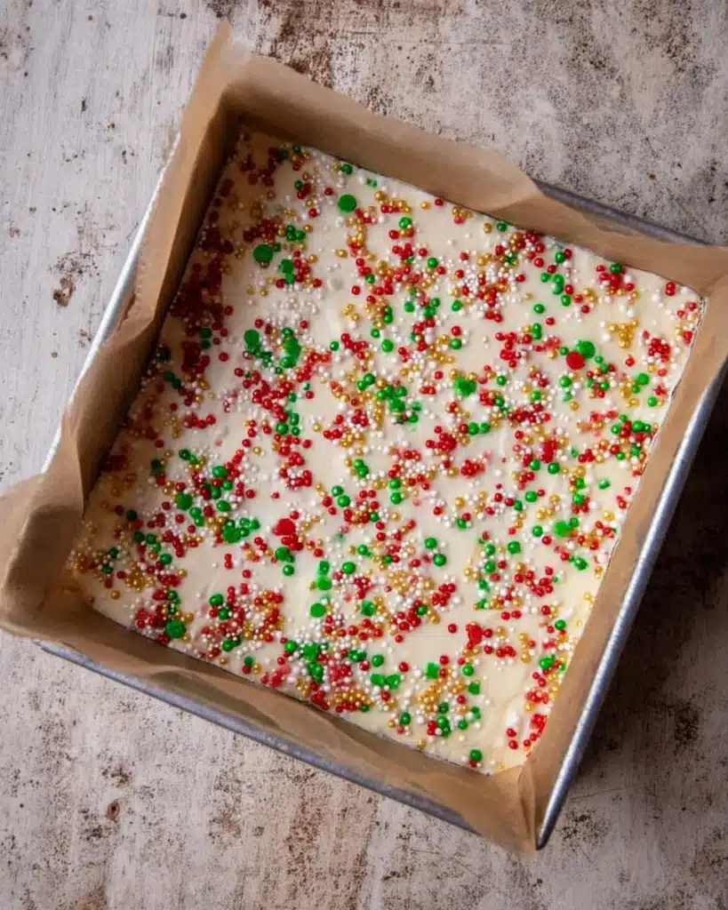 Christmas Sugar Cookie Bars (Soft, Chewy & Frosted) 5 Frosted Christmas sugar cookie bars with red, green, and gold sprinkles in a baking pan