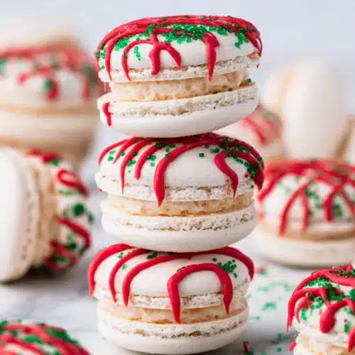 Stacked Christmas Tree Cake Macarons with red icing and green sprinkles on marble surface