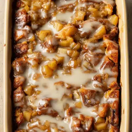 Warm cinnamon roll apple bake topped with vanilla icing in a ceramic dish