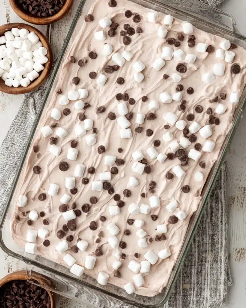 Finished cocoa poke cake topped with whipped cream, marshmallows, and chocolate chips
