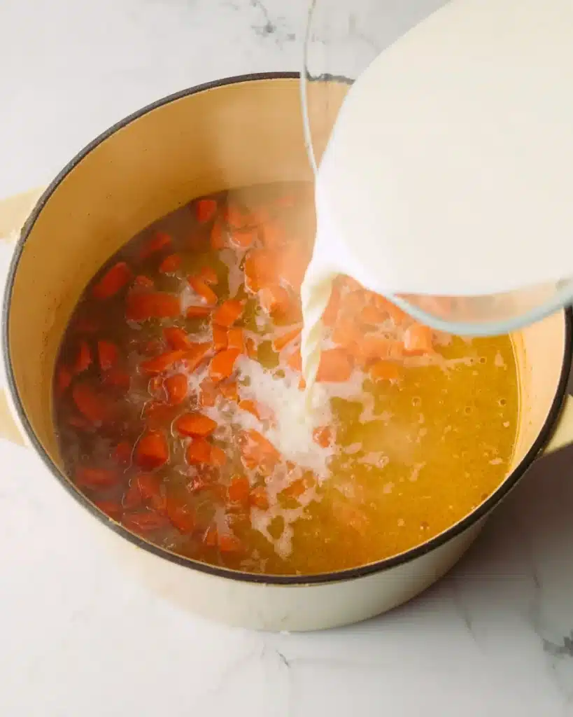 Creamy Vegetable Soup 4 Pouring milk into simmering broth with carrots to make creamy vegetable soup