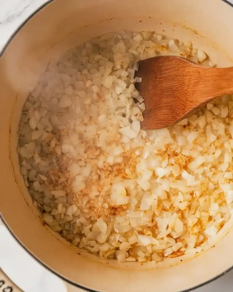 Creamy Vegetable Soup 2 Diced onions sautรฉing in butter in a beige pot with a wooden spoon for creamy vegetable soup