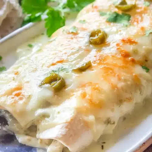 Creamy white chicken enchiladas topped with melted cheese and green chiles on a white plate
