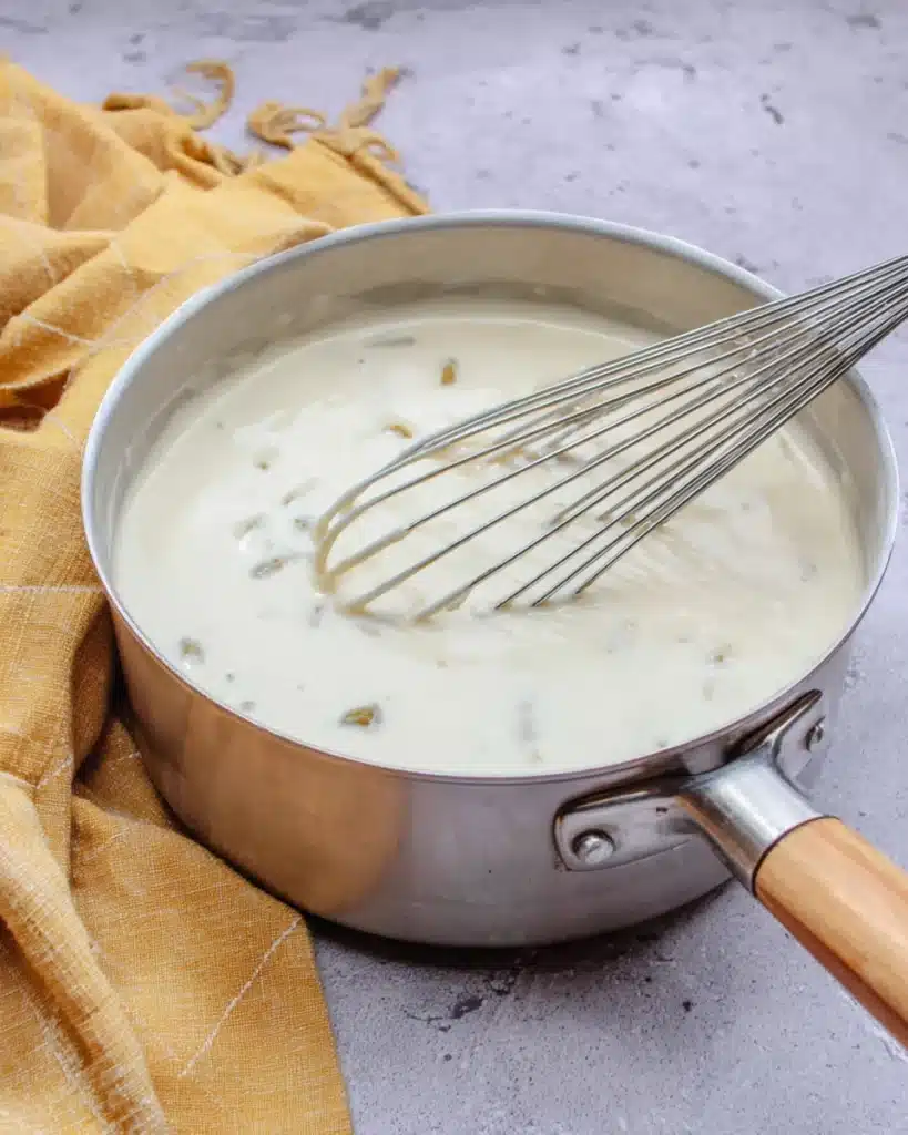 Creamy white sauce with green chiles in a saucepan for chicken enchiladas