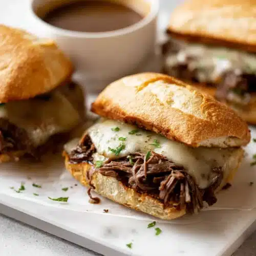 Crockpot French Dip Sandwiches with melted cheese on toasted ciabatta roll and au jus sauce