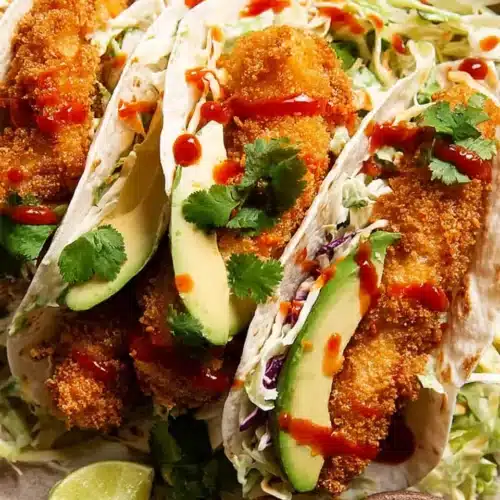 Crunchy chicken taco fingers with avocado, slaw, and sriracha in soft tortillas
