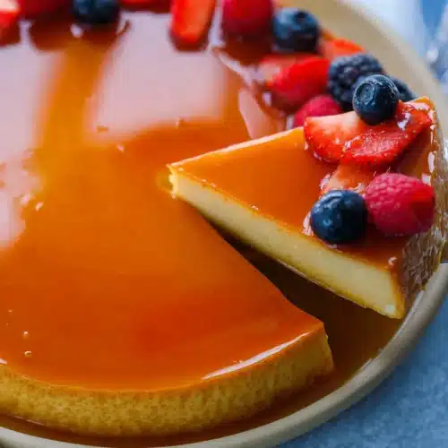 Flan Recipe (Perfect Creamy Caramel Custard for Christmas) 3 Creamy caramel Flan Recipe with glossy topping and fresh berries, with one slice being lifted.