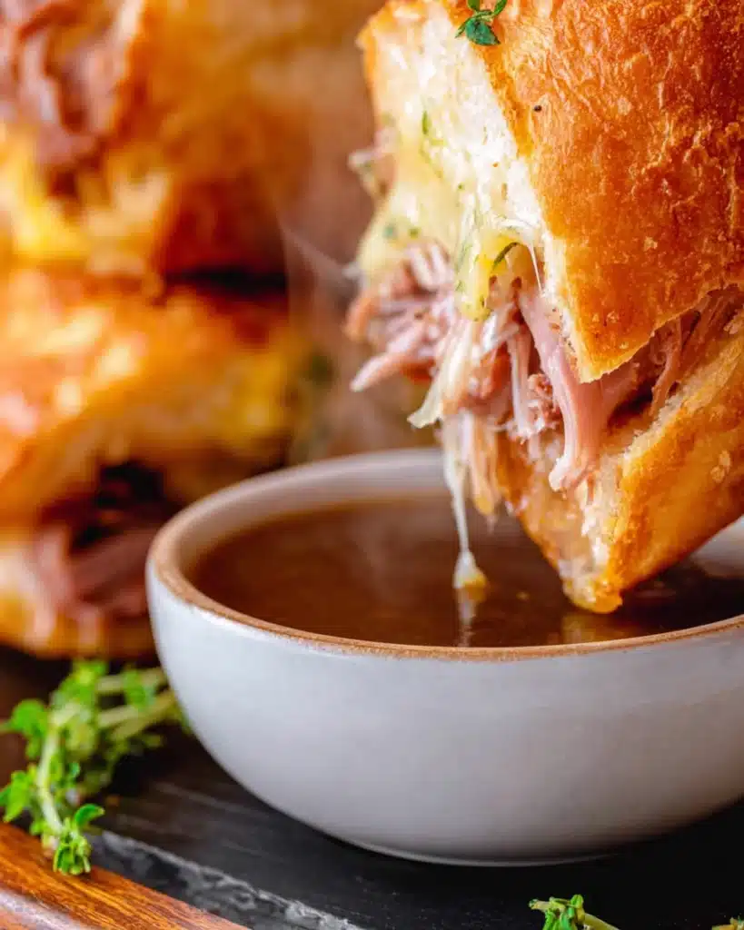 French Dip Slider dipped into au jus sauce with melted cheese and roast beef