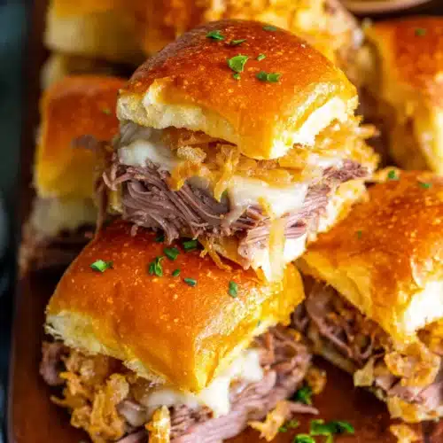 Golden French dip sliders with roast beef, melted cheese, and crispy onion topping on a wooden board