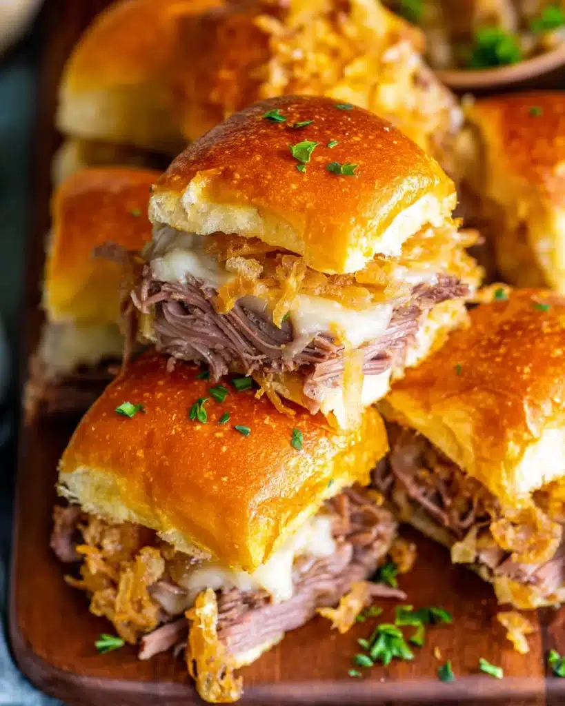 Golden French dip sliders with roast beef, melted cheese, and crispy onion topping on a wooden board