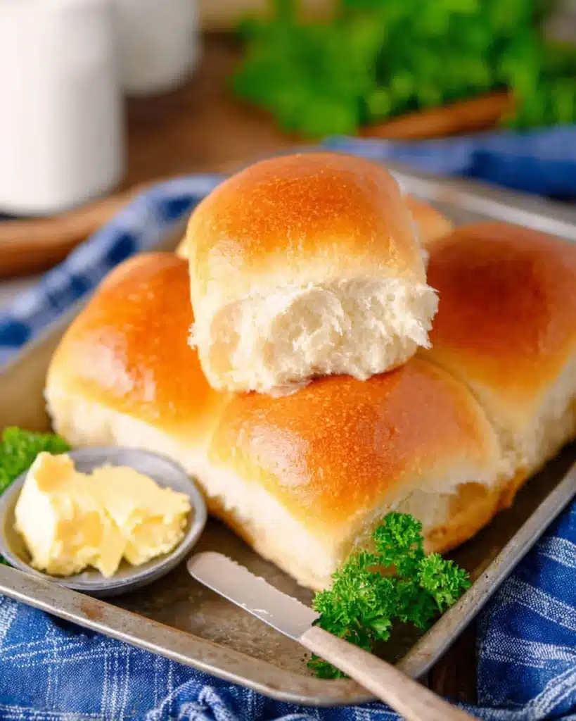 Golden homemade dinner rolls on a tray with butter and parsley