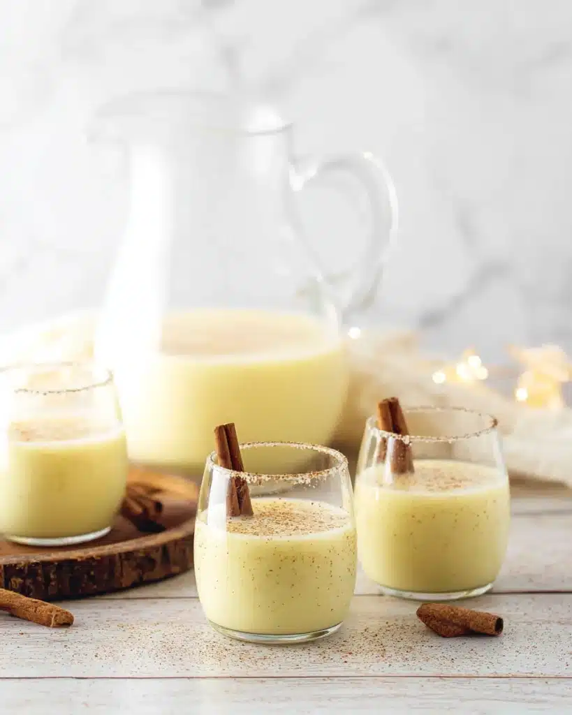 Homemade Eggnog Recipe 2 Homemade eggnog in glass pitcher and cups with cinnamon sticks