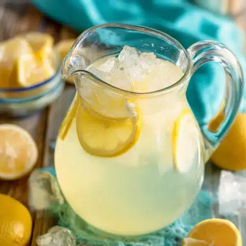 Homemade lemonade in a glass pitcher with ice and lemon slices on a rustic table