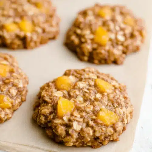 Soft peach oatmeal breakfast cookies with juicy peach chunks on parchment paper