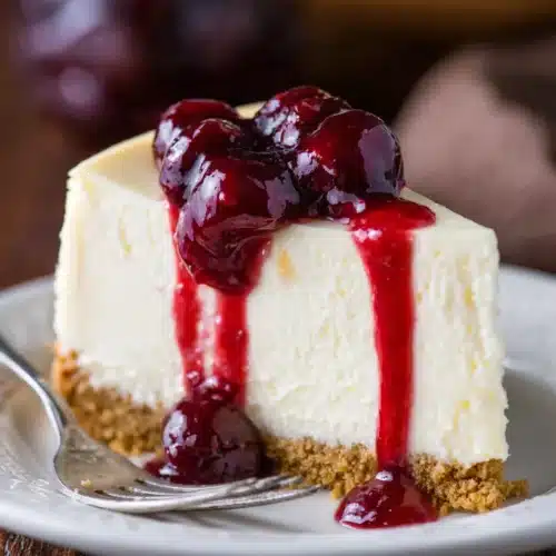 Slice of Perfect Cheesecake with cherry topping on white plate