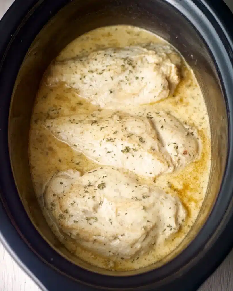 Easy 4-Ingredient Ranch Chicken Crock Pot Recipe 3 Chicken breasts cooking in creamy ranch sauce inside a slow cooker