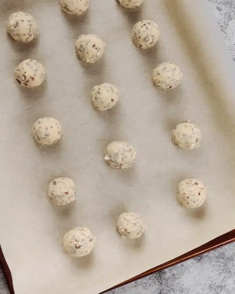 Unbaked Russian Tea Cakes dough balls on parchment-lined baking sheet