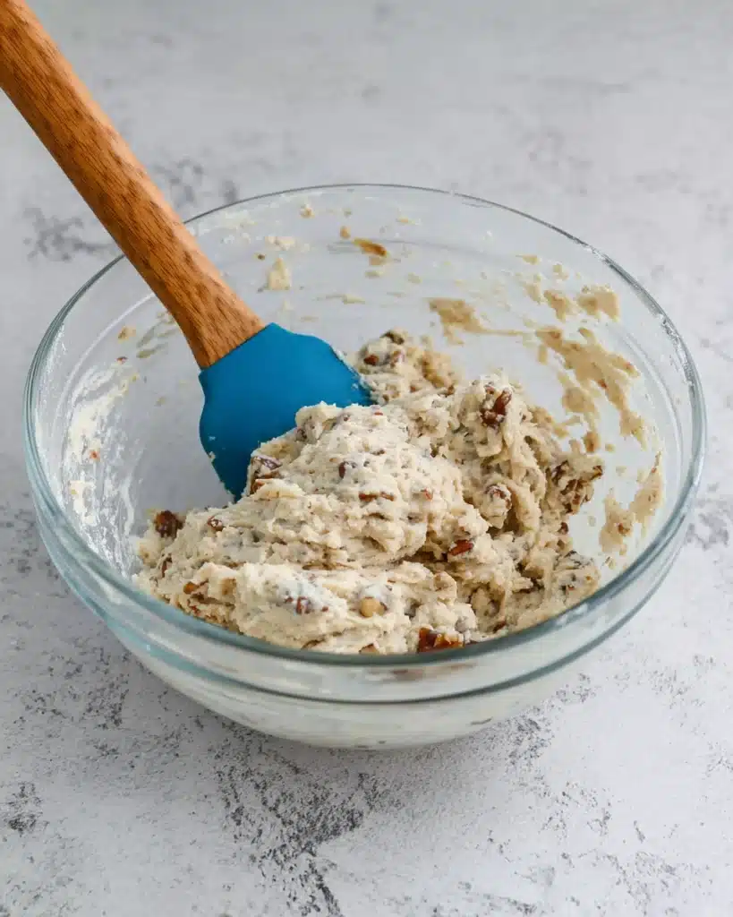 Mixing Russian Tea Cakes dough with chopped pecans in a glass bowl
