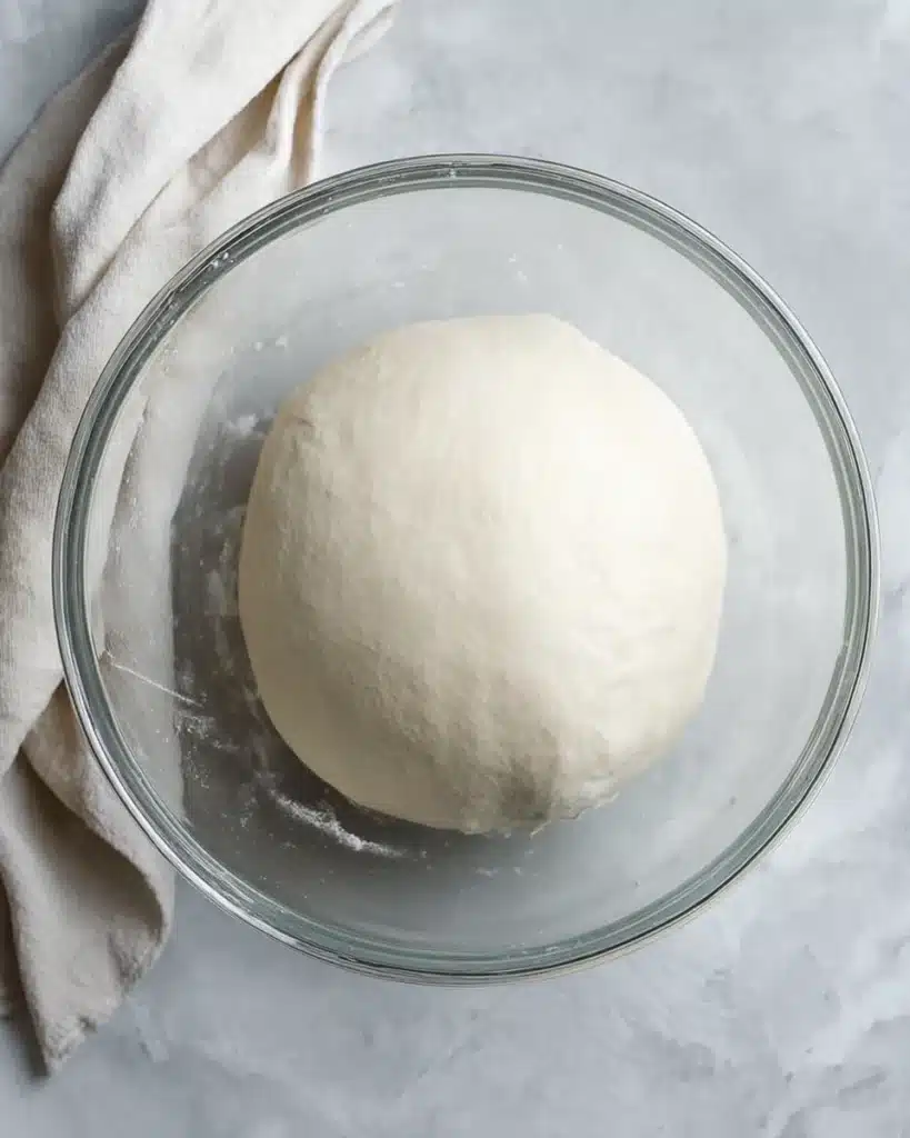 Risen sourdough dough in glass bowl after kneading