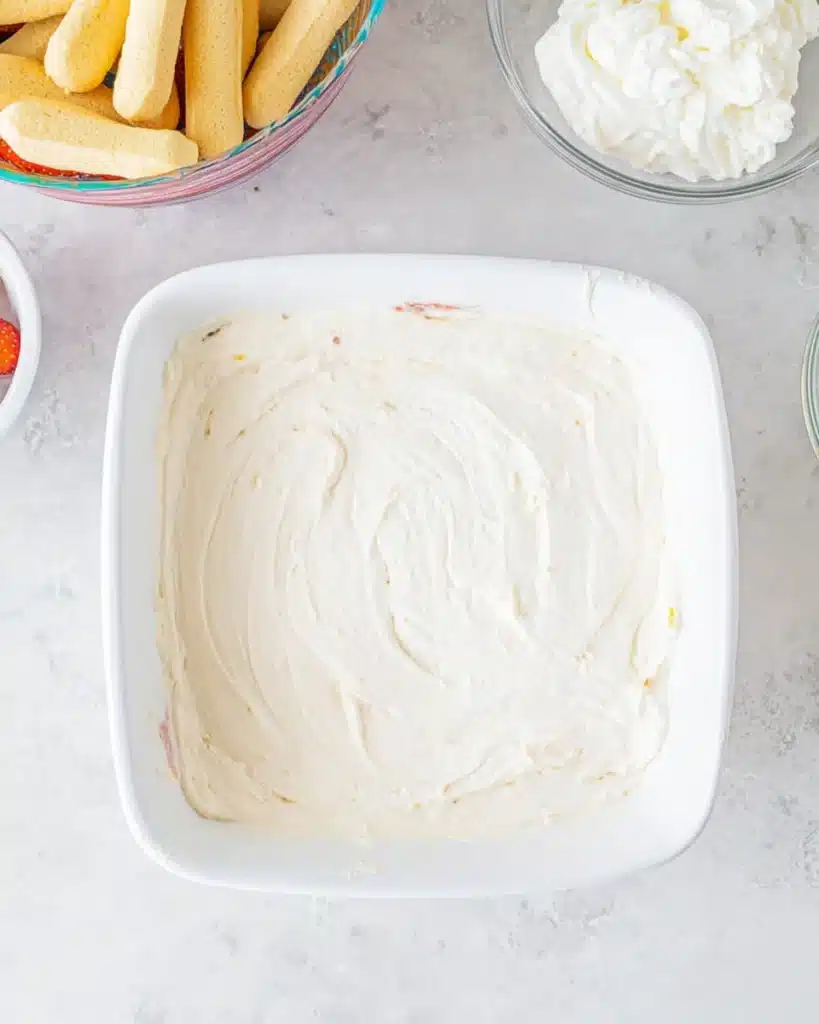 Cream layer of strawberry tiramisu spread in white baking dish