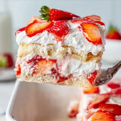 Slice of strawberry tiramisu with whipped cream and fresh strawberries in a white dish