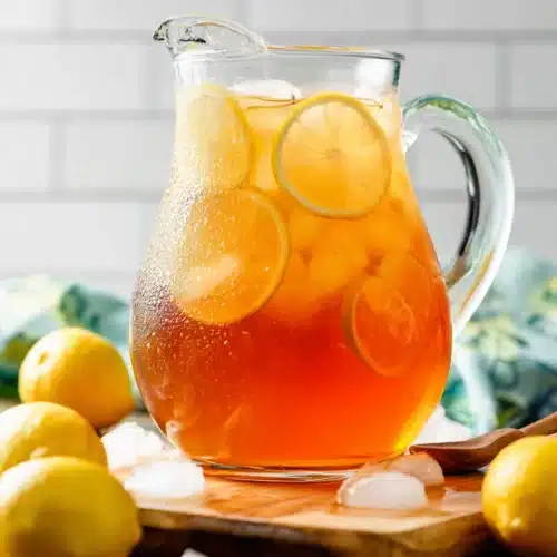 Sweet Tea Recipe – The Perfect Refreshing Southern Drink 6 Glass pitcher of sweet tea with lemon slices and ice on wooden board