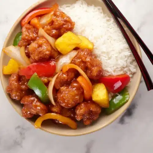 Sweet and sour chicken with rice, peppers, and pineapple in a beige bowl