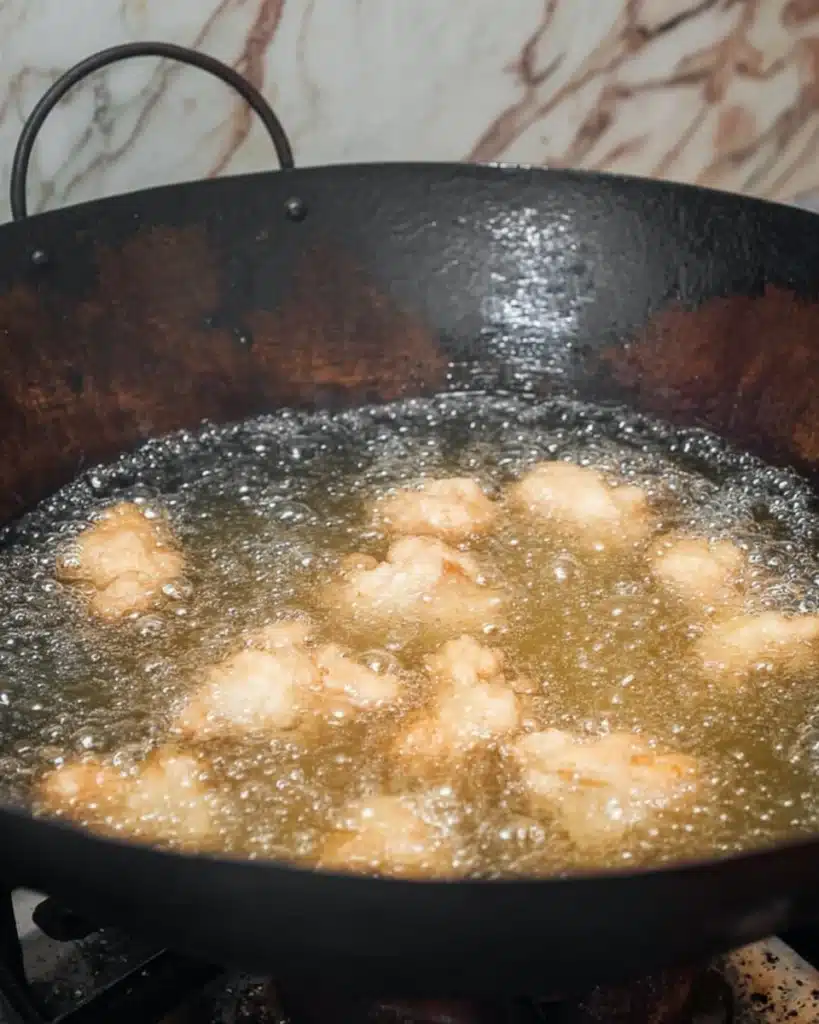 Chicken frying in hot oil inside a black wok for sweet and sour chicken recipe