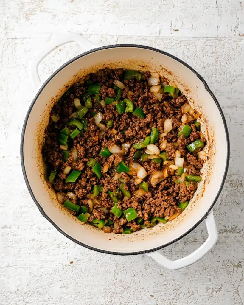 Ground beef with onions and peppers cooking in a white Dutch oven for taco soup