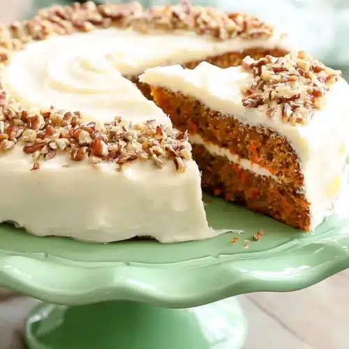 The BEST Carrot Cake (Christmas Favorite) 6 The BEST Carrot Cake with cream cheese frosting and chopped nuts on a green cake stand