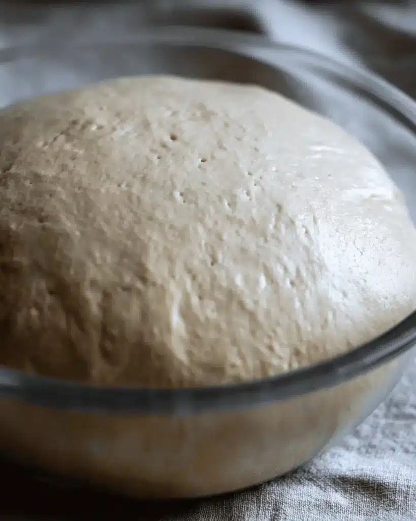 Risen sourdough bagel dough in a glass bowl after overnight fermentation