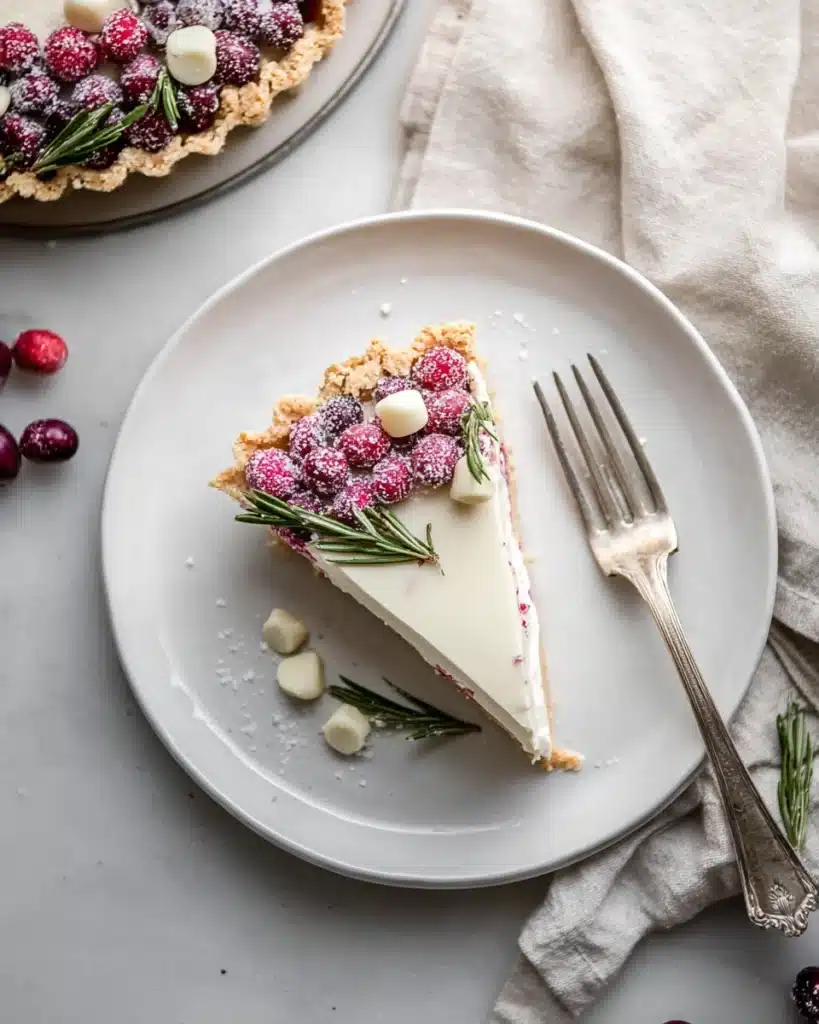 White chocolate cranberry tart slice on white plate with sugared cranberries