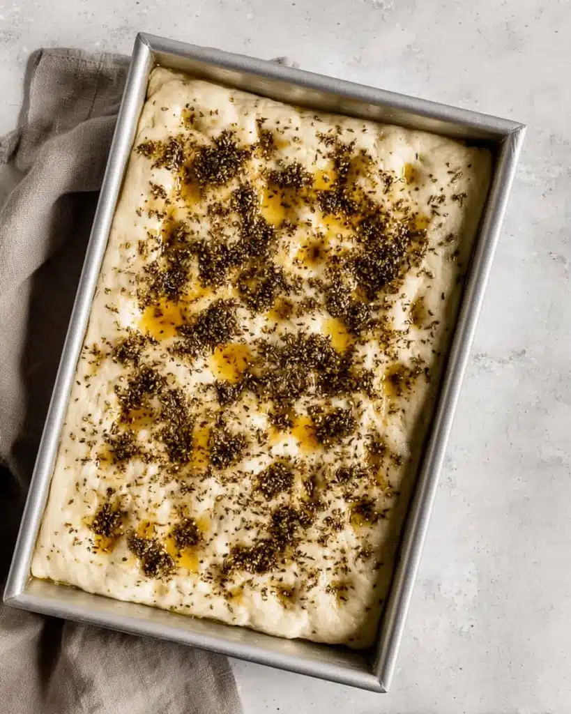 Focaccia dough topped with za’atar and olive oil in a baking pan