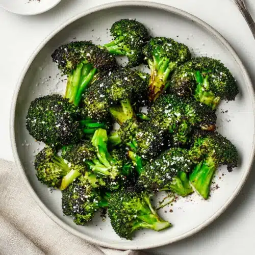 Crispy air fryer broccoli in a white bowl with sea salt and pepper on a light background