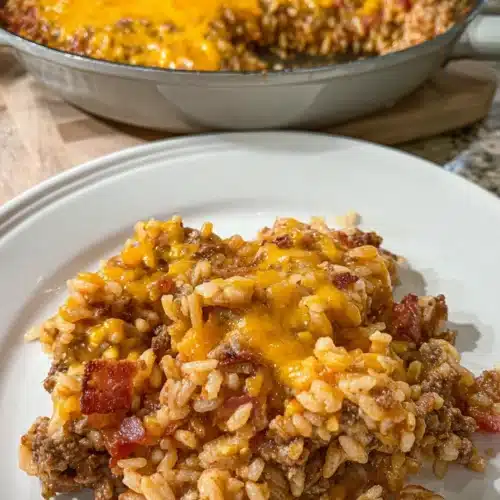 Plated bacon cheeseburger rice skillet with melted cheddar and bacon on white dish