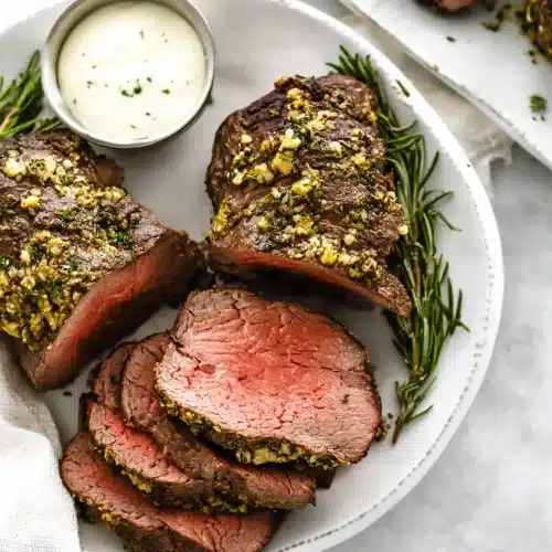 Juicy beef tenderloin roast slices with garlic herb crust on a white plate