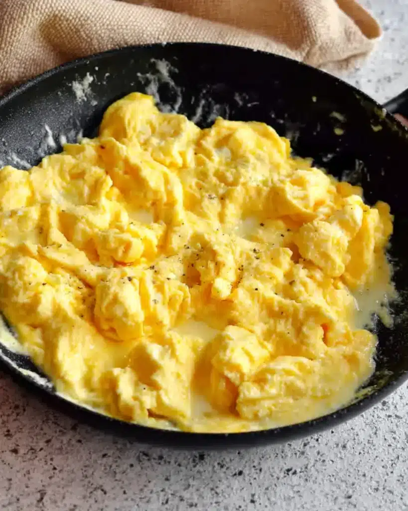 The Best Breakfast Burritos (Hearty, Cheesy & Freezer-Friendly!) 3 Soft scrambled eggs cooking in a black skillet for breakfast burritos