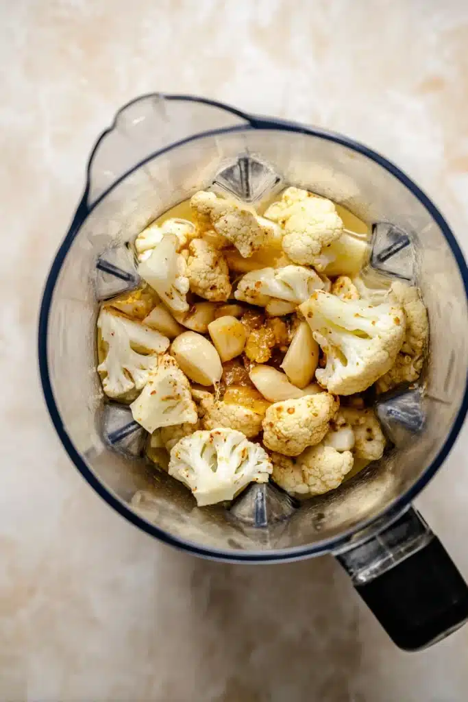Blender filled with roasted cauliflower, garlic, and broth for cheddar cauliflower soup