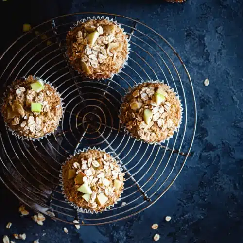 Cinnamon Apple Oatmeal Muffins 5 Cinnamon apple oatmeal muffins on a wire cooling rack with oats and apple pieces