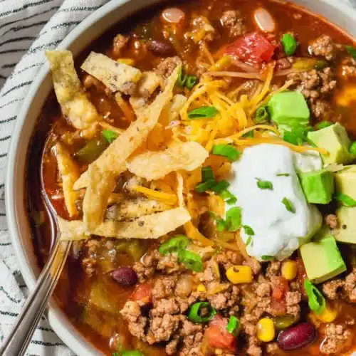 Easy Taco Soup with beef, beans, avocado, and sour cream in a white bowl