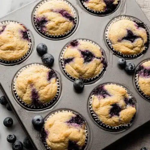 Homemade blueberry protein muffins baked in a muffin pan with juicy blueberries and soft golden tops